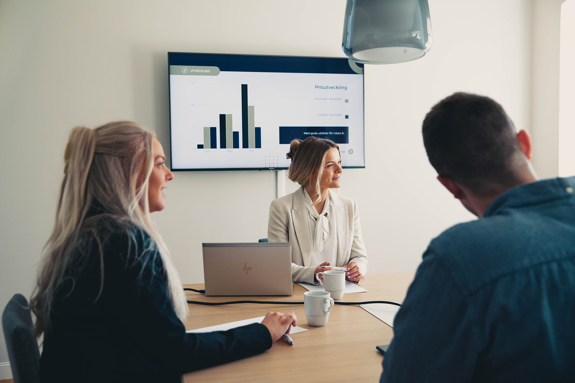 Business meeting with three people discussing charts on screen